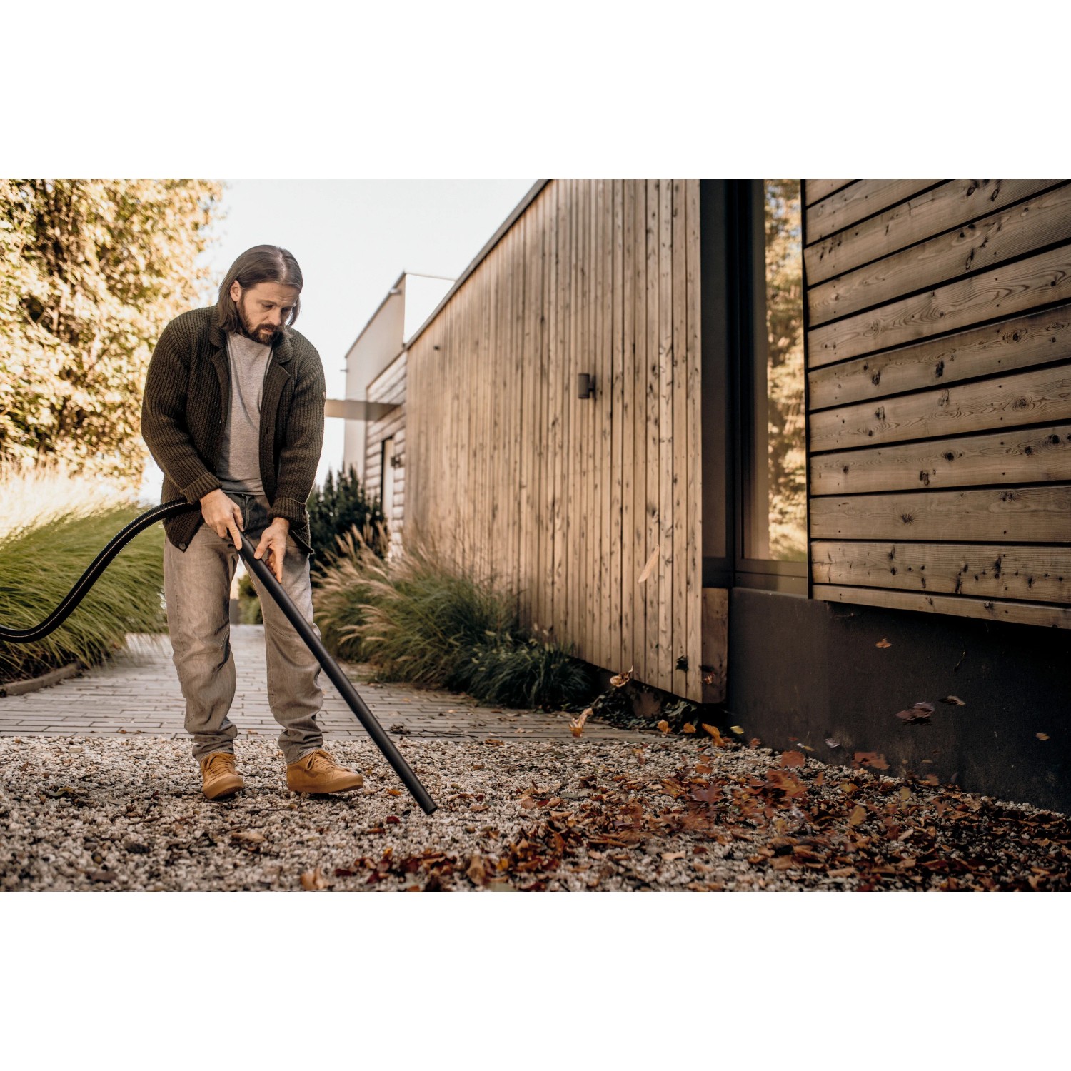 Mann saugt Laub mit Kärcher WD 1 Classic Nass-Trockensauger vor Holzhaus.