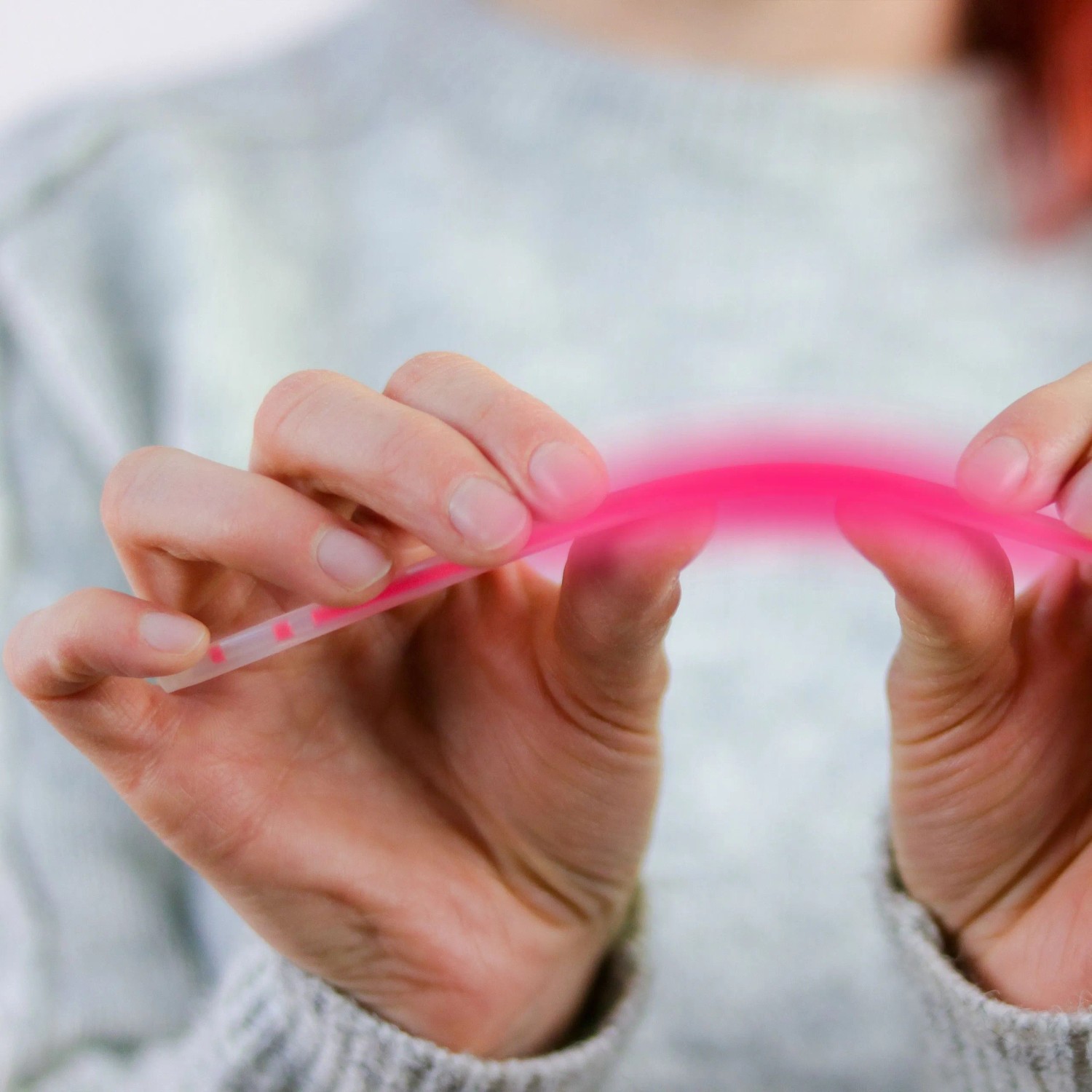 Hände biegen ein pinkes Knicklicht, das zu leuchten beginnt. Bunter Leuchtstab für Partys, Festivals & Kinder.