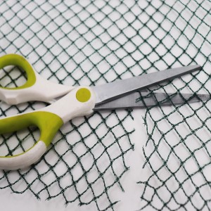 Dunkelgrünes Aquagart Teichnetz wird mit einer Schere zugeschnitten.
