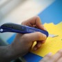 LUX Präzisionsmesser Classic schneidet gelbes Papier. Blau-schwarzes Bastelmesser im Einsatz.