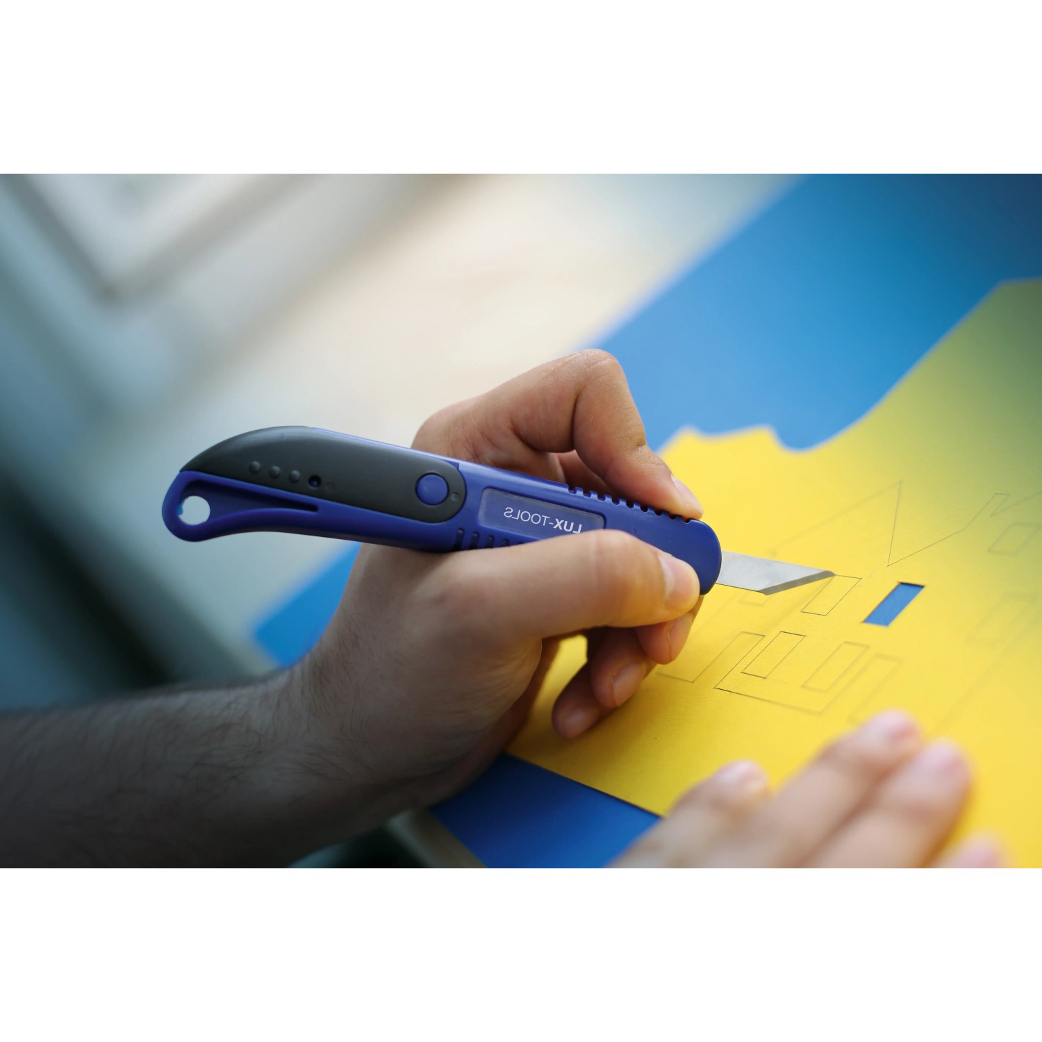 LUX Präzisionsmesser Classic schneidet gelbes Papier. Blau-schwarzes Bastelmesser im Einsatz.