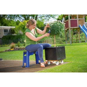 Frau sitzt auf blauem LUX Gartenhocker mit Kniekissen und schneidet Pflanze im Garten.