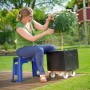 Frau sitzt auf blauem LUX Gartenhocker mit Kniekissen und schneidet Pflanze im Garten.