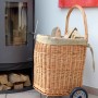 Kaminholzwagen aus Weide mit Rädern und Jute-Auskleidung neben Kaminofen.