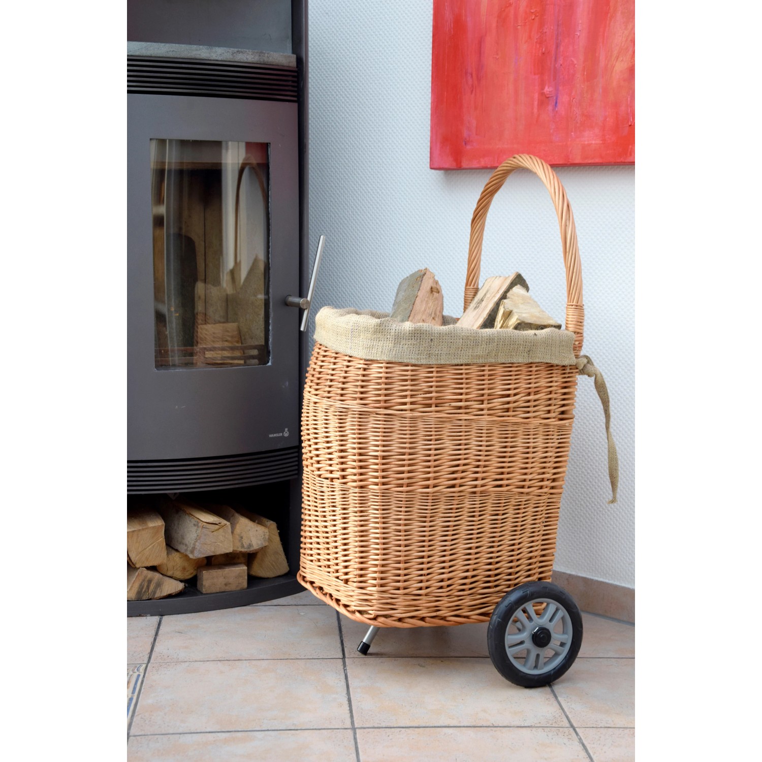 Kaminholzwagen aus Weide mit Rädern und Jute-Auskleidung neben Kaminofen.