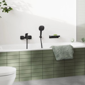 Mattschwarze Grohe Einhand-Wannenarmatur Dice mit Handbrause an weißer Wand über Badewanne.