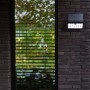 Schwarze Lutec LED Solar-Wandleuchte Tuda mit Bewegungsmelder an dunkler Backsteinwand.