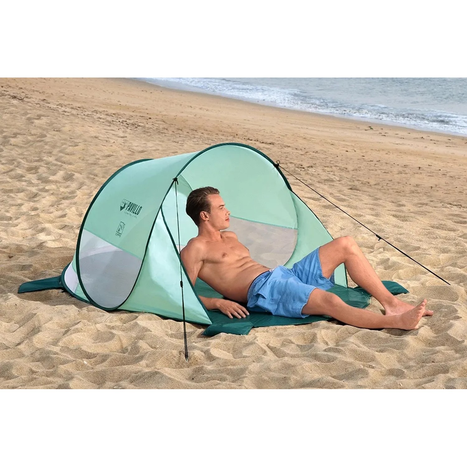 Pavillo Strandmuschel Beach Quick 2: Türkisfarbenes Pop-Up Zelt mit liegendem Mann am Strand.