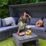Dunkelbraunes Beliani Lounge Set CORTE aus Polyrattan mit grauen Kissen, Sonnendach und Couchtisch im Garten. Frau entspannt.