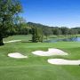 Grüner Golfplatz mit mehreren Sandbunkern, See und Bäumen. Heller Sand in den Bunkern. Schüttgüter.