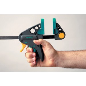 Hand hält wolfcraft Einhandzwinge EHZ Pro 65-150. Spannwerkzeug mit grau-grünem Griff und gelbem Auslöser.