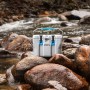 Graue Lifetime Kühlbox (26,5 Liter) mit blauem Griff und Verschlüssen auf Steinen am Fluss.