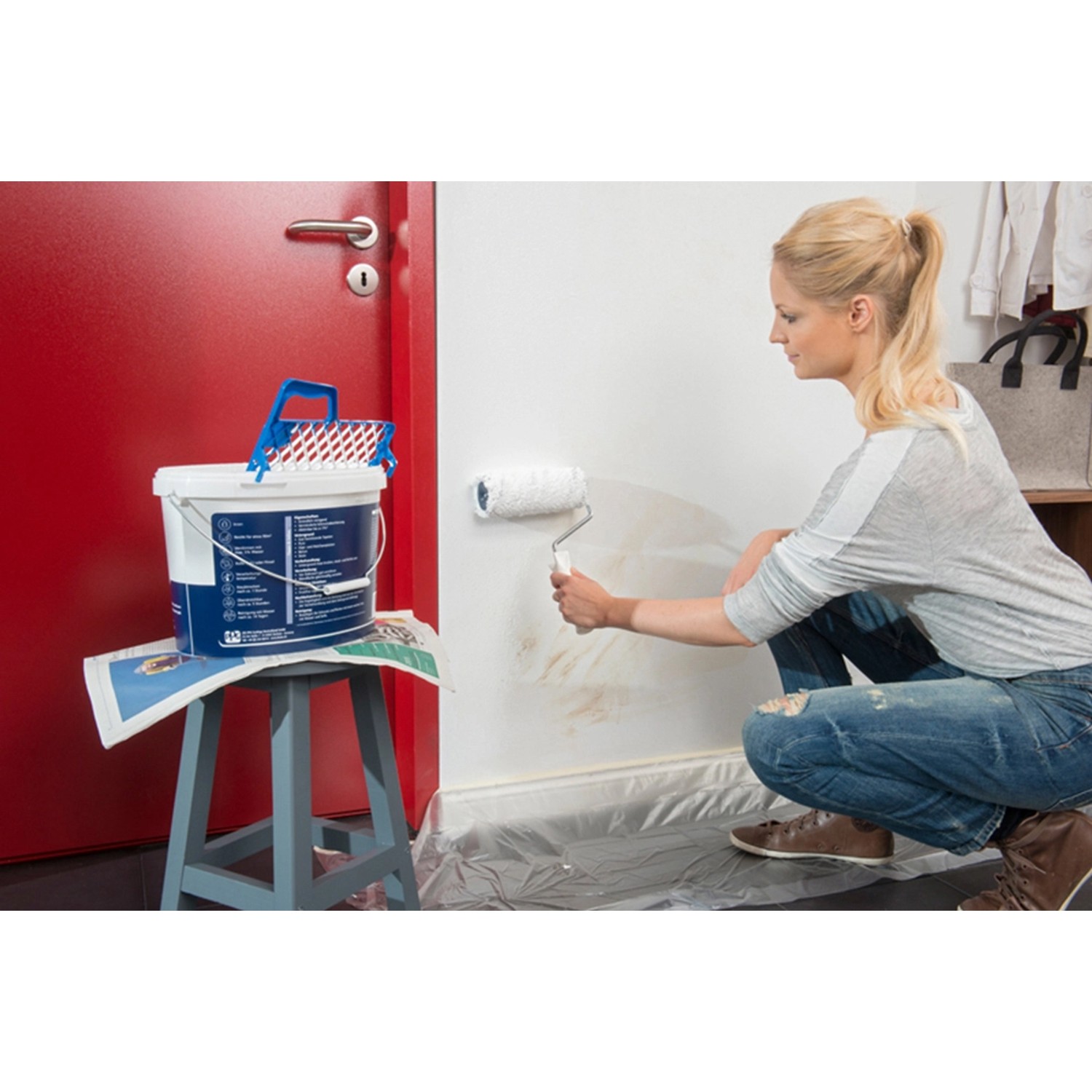 Frau streicht Wand mit Histor Clean Wandfarbe Weiß seidenmatt, 10 l Eimer steht bereit.