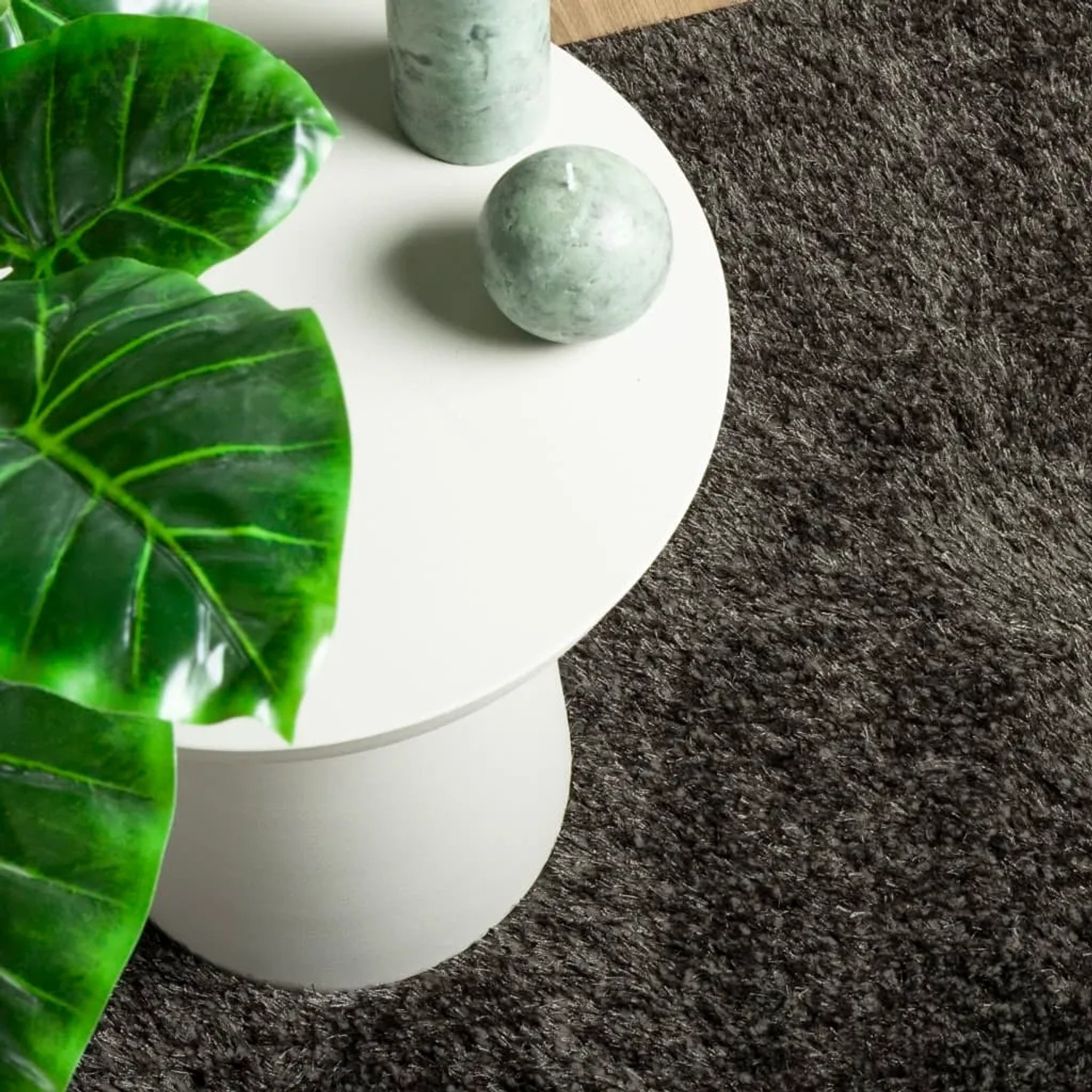 Anthrazitfarbener Hochflor Teppich Istan (120x170 cm) neben einem Tisch mit Dekoration.