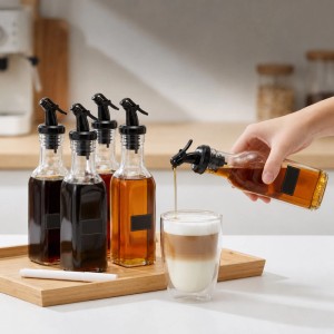 Relaxdays Ölflaschen 12er Set aus transparentem Glas mit schwarzen Ausgießern. Eine Flasche gießt Sirup in ein Getränk auf einem Holztablett in der Küche.