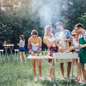 Fröhliche Gruppe grillt im Garten; weiße klappbare Barhocker und Stehtische für Outdoor-Feiern.