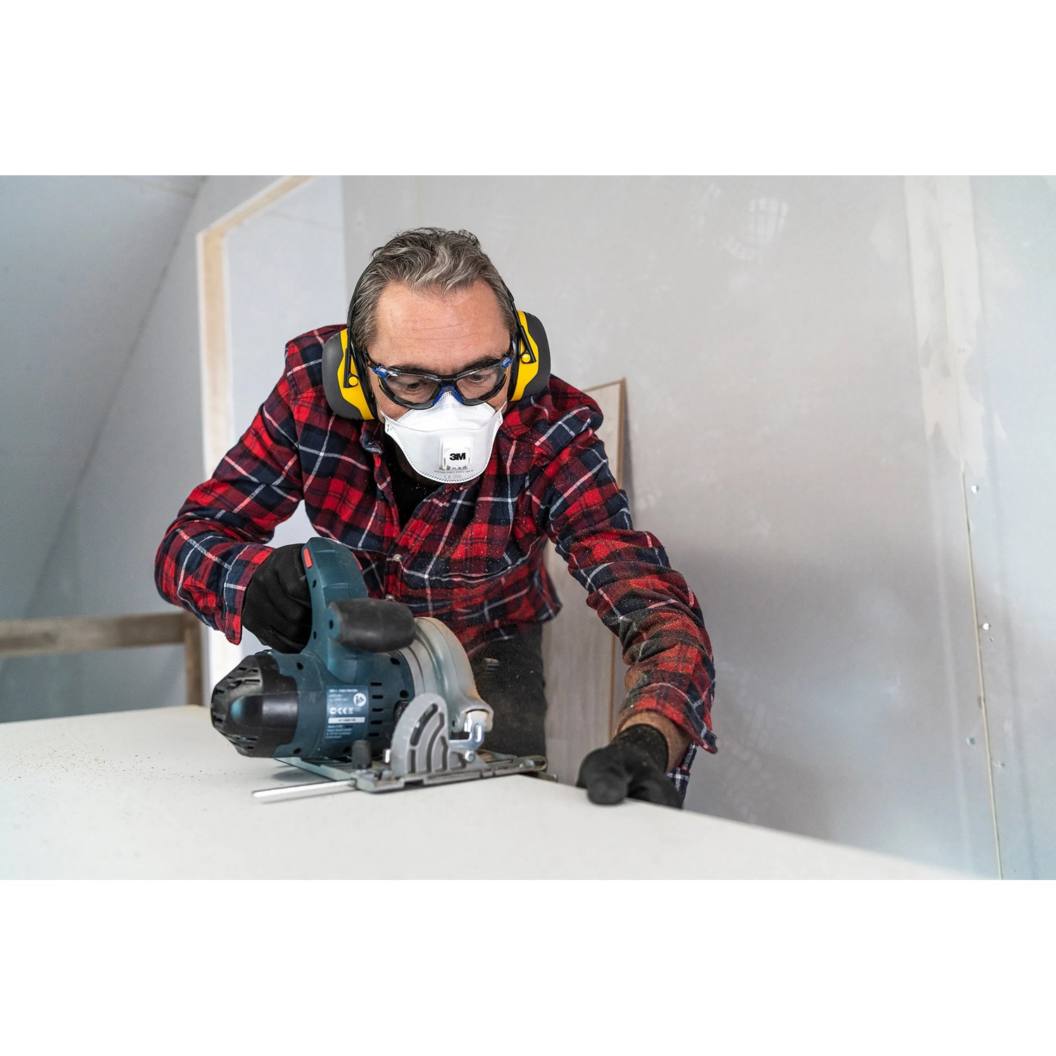 Mann mit 3M Peltor Kapselgehörschutz X2A, Schutzbrille und Maske beim Sägen.