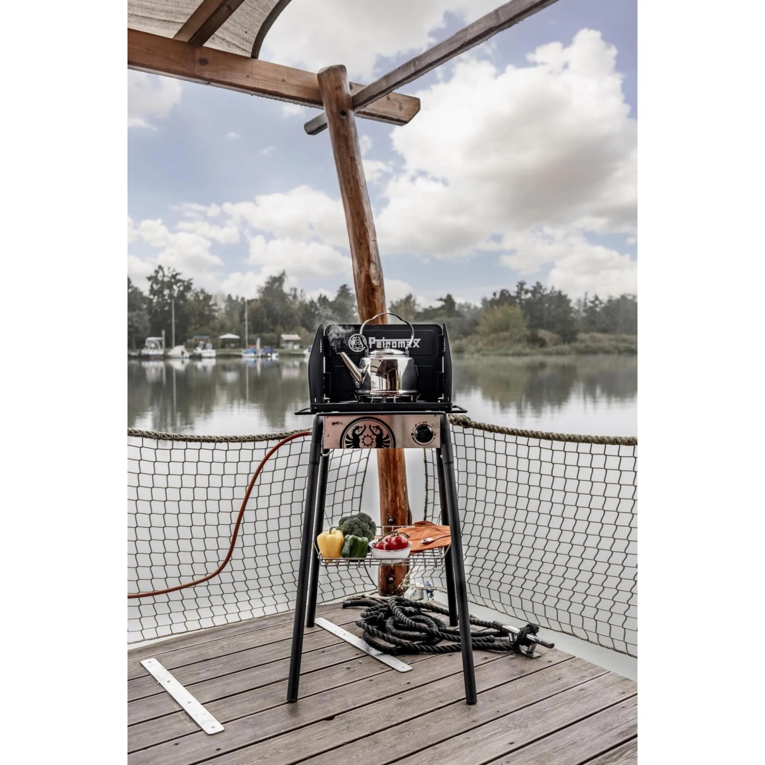 Petromax Feuertopf-/Gastisch FE45 mit Ablagekorb 40 cm und Grillutensilien auf einer Terrasse am Wasser.