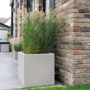 Quadratischer Pflanzkübel QUBO 60 Stone aus Kunststoff mit Ziergras auf Terrasse vor Ziegelwand. Modernes Design.