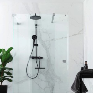 Schwarzes Schöner Wohnen Duschsystem Glaia mit Thermostat und Kopf- sowie Handbrause vor Marmorwand.
