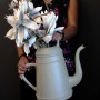 Olivgraue Gießkanne Lungo 12L mit Blumen, gehalten von einer Person.