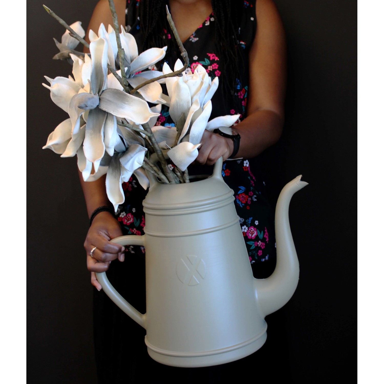 Olivgraue Gießkanne Lungo 12L mit Blumen, gehalten von einer Person.