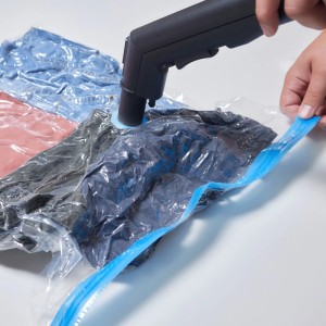 Hand saugt Luft aus transparentem Vakuumbeutel mit Kleidung per Staubsauger. Blauer Reißverschluss für platzsparende textile Aufbewahrung.