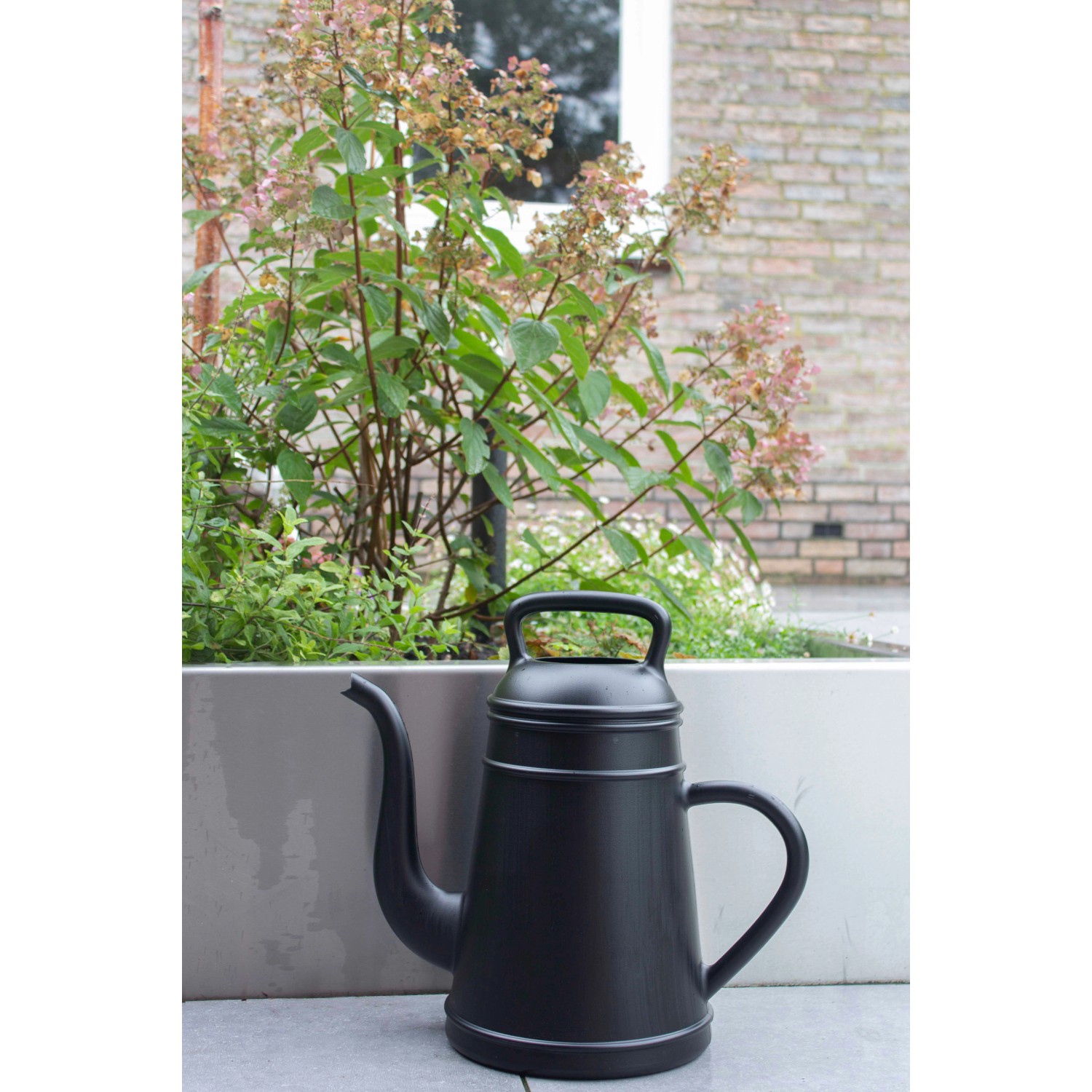 Schwarze Xala Gießkanne Lungo (12 l) vor Pflanzenkübel. Design-Gießkanne für Garten und Zuhause.