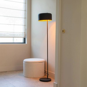 Schwarze QAZQA Stehlampe Jinte mit goldenem Innenleben neben einem Hocker.