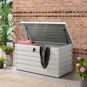 Weiße Juskys Metall Aufbewahrungsbox Limani mit geöffnetem Deckel, Kissen und Decke im Garten.