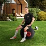 Mann sitzt auf schwarzem Sitting Ball Hocker FCB (120l) im Garten, Fußball liegt daneben.