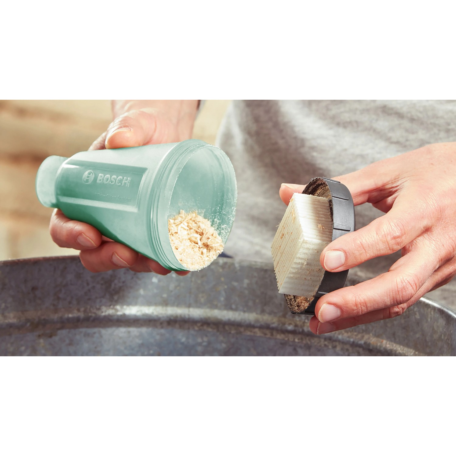 Hand entleert Staubfangbox des Bosch Akku-Multischleifers UniversalSander mit Sägespänen. Staubreduzierung.