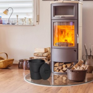 Schwarzer Relaxdays Ascheeimer aus Stahl mit Deckel und Henkel, vor brennendem Kamin. Zubehör für Kamine & Öfen.