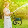 Frau bewässert Garten mit grünem Schlauch. Im Hintergrund: schwarzer, fahrbarer Relaxdays Gartenschlauchwagen aus Stahl.