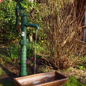 Grüne TRUTZHOLM Schwengelpumpe aus Gusseisen mit Pumpenständer im Garten, Wasser läuft.