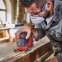 Einhell Akku-Faustschleifer TE-OS 18/113 Li-Solo im Einsatz auf Holz. Kompaktes Design, rot-schwarz.