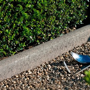 Grauer, abgerundeter Kann Rasenkantenstein aus Beton (30x100x5 cm) als Beeteinfassung im Garten.