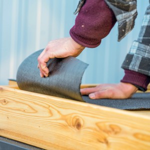 Graue Bitumenschweißbahn PYE PV 200 S5 wird verlegt. Dachabdichtung mit Beschieferung.