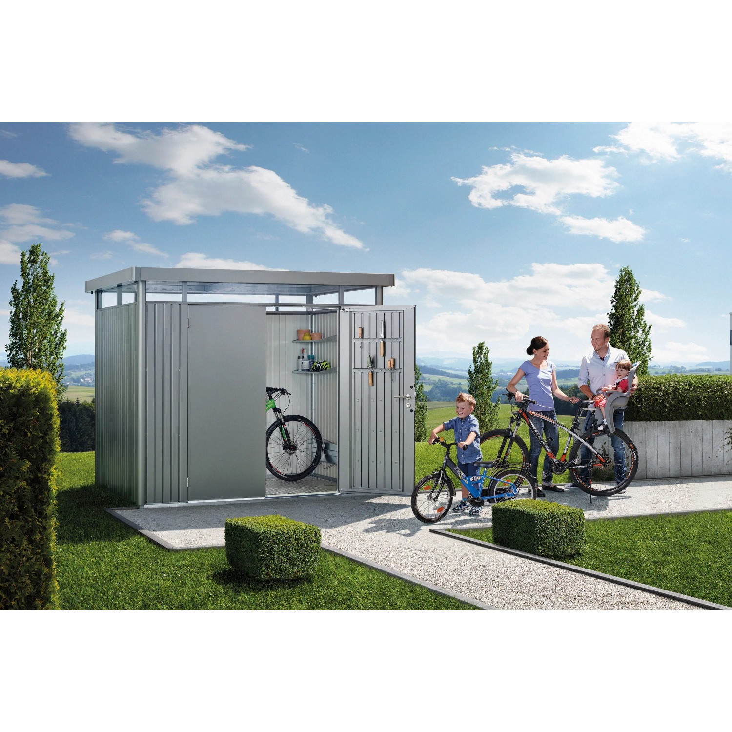 Biohort HighLine Metall-Gerätehaus in Quarzgrau mit Fahrrädern und Familie im Garten.
