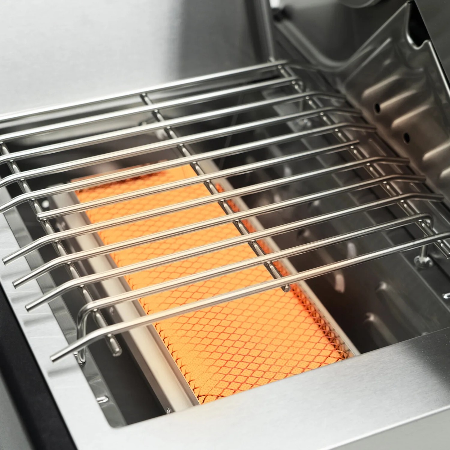 Detailaufnahme: Sear-Burner des Taino Platinum Yamara Gasgrills. Edelstahlrost über orangefarbener Keramik.