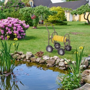 Brauner Relaxdays Gartenschlauchwagen aus Stahl mit gelbem Schlauch und 4 Vollgummirädern im Garten am Teich.