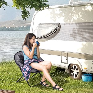 Frau sitzt entspannt im grauen Outsunny Campingstuhl aus Metall und Polyester vor Wohnwagen.