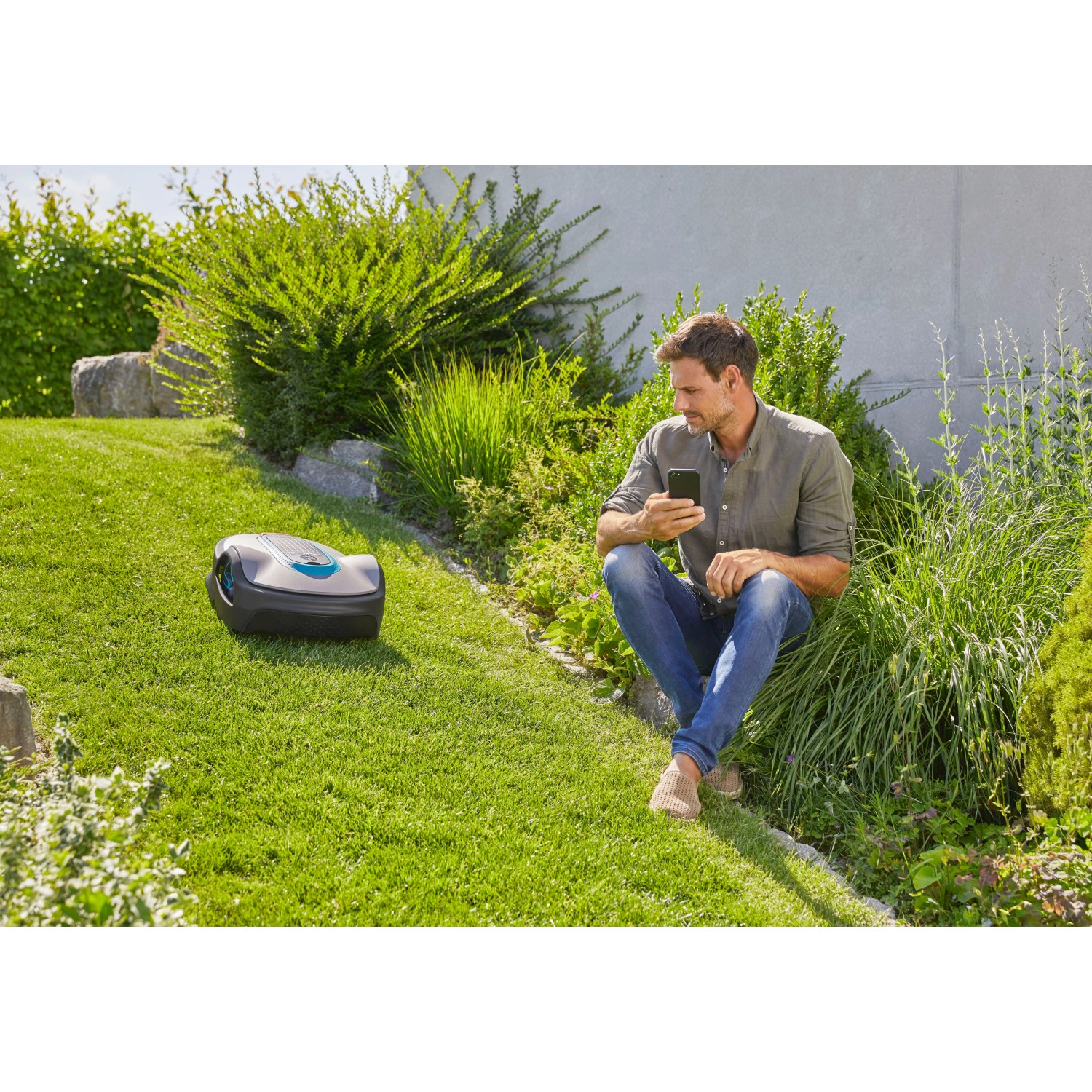 Gardena smart Sileno life Mähroboter mit Gateway und Mann mit Smartphone im Garten.