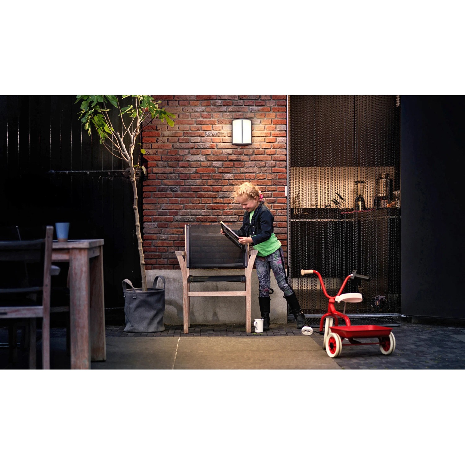 Philips myGarden LED-Außenwandleuchte Stock in Anthrazit an einer Backsteinwand mit Kind und Spielzeug.