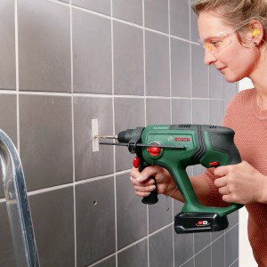 Frau bohrt mit Bosch Akku-Bohrhammer UniversalHammer 18V in geflieste Wand.