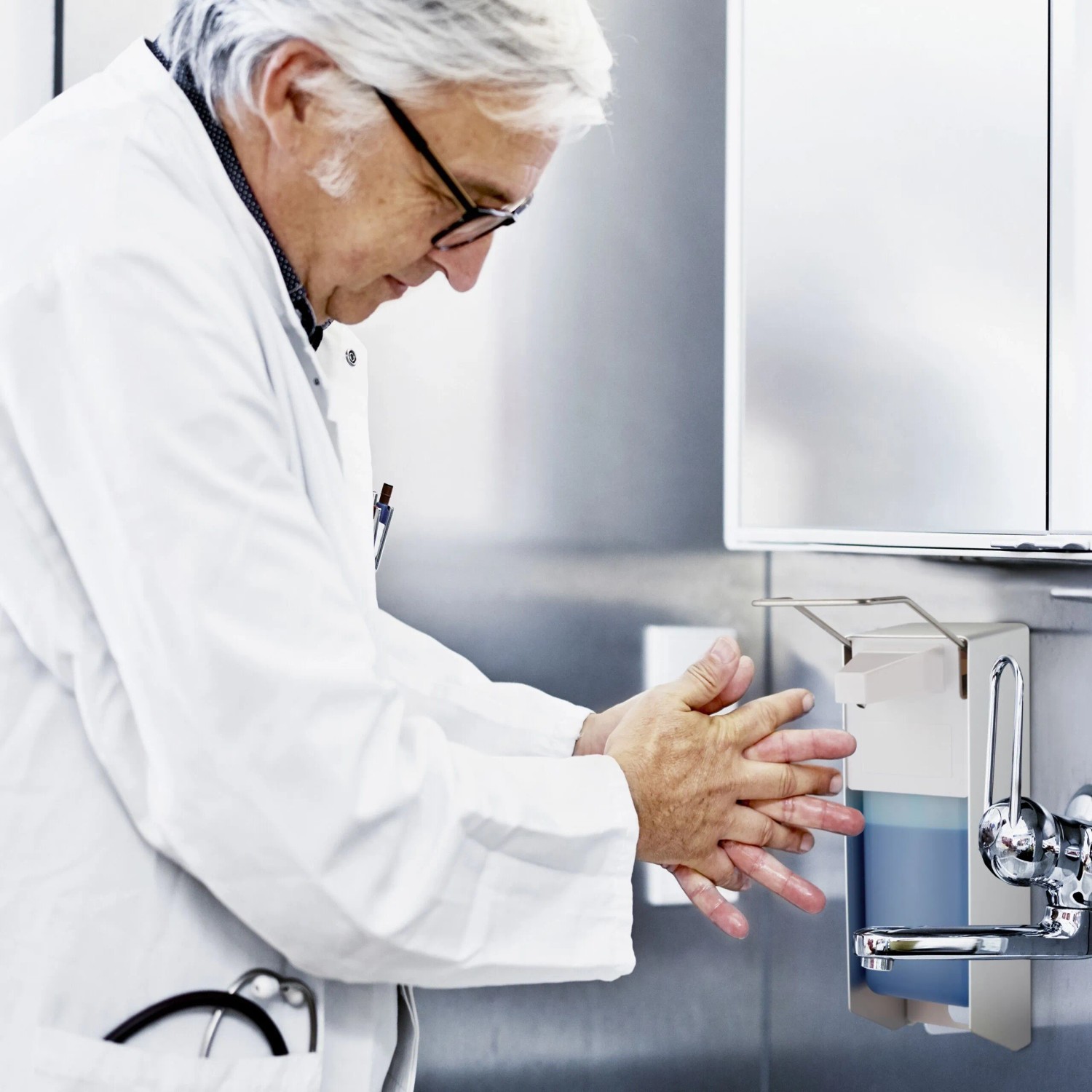 Arzt nutzt silber-weißen Wand-Desinfektionsspender mit Hebel. Hygienische Seifenentnahme für Klinik, 1000 ml.