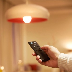 Hand hält schwarze Philips Fernbedienung, steuert smarte dimmbare Leuchte. Programmierbare Lichtsteuerung für Ihr Zuhause.