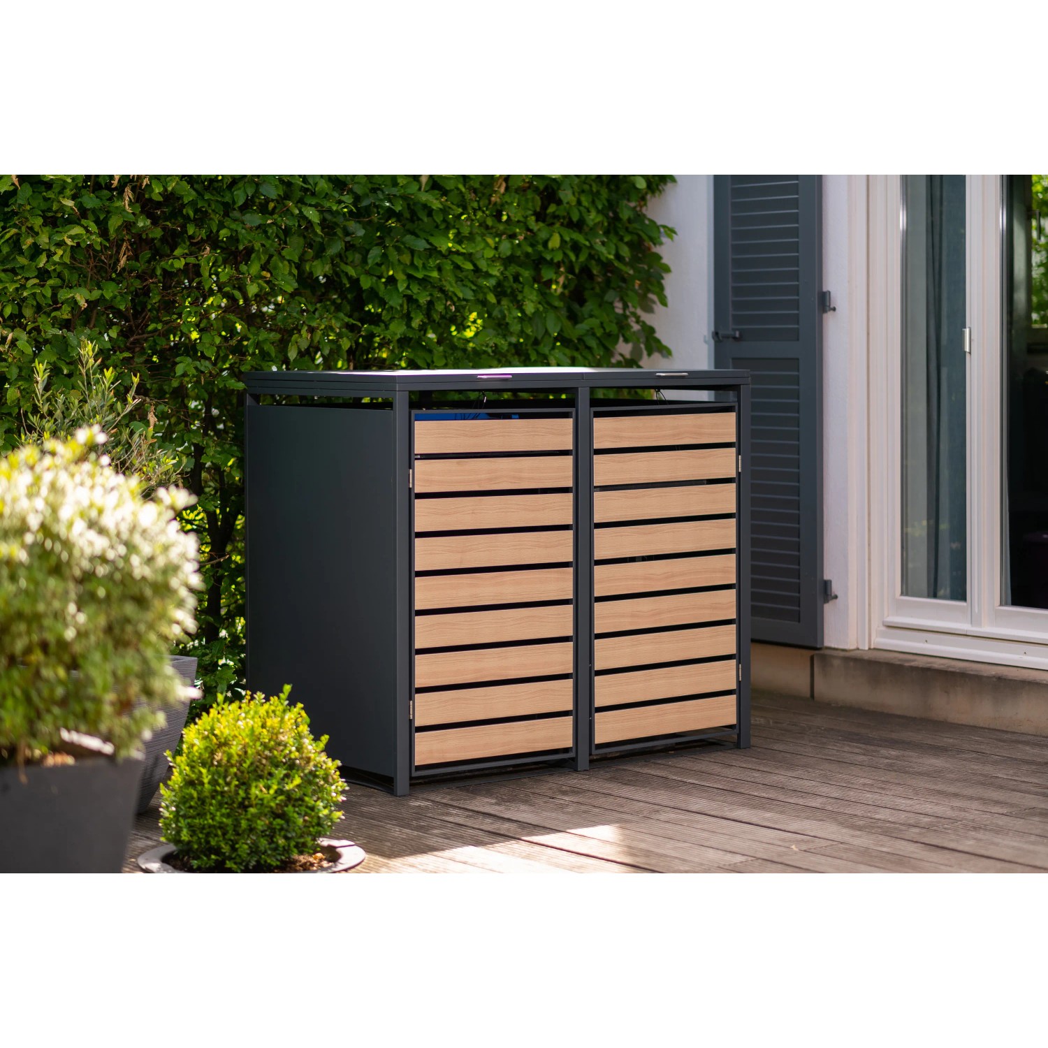 Westmann Mülltonnenbox für 2 Tonnen (240 l) in Holzoptik vor Hauswand mit Pflanzen.