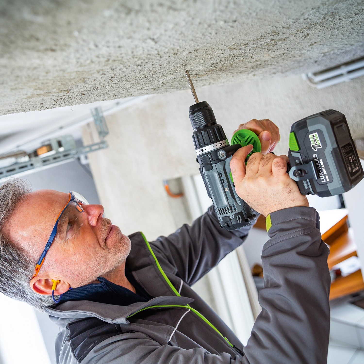 Mann bohrt mit LUX Akku-Schlagbohrschrauber A-BS-20/S in Decke. Inkl. Zusatzhandgriff und Gürtelhalter.