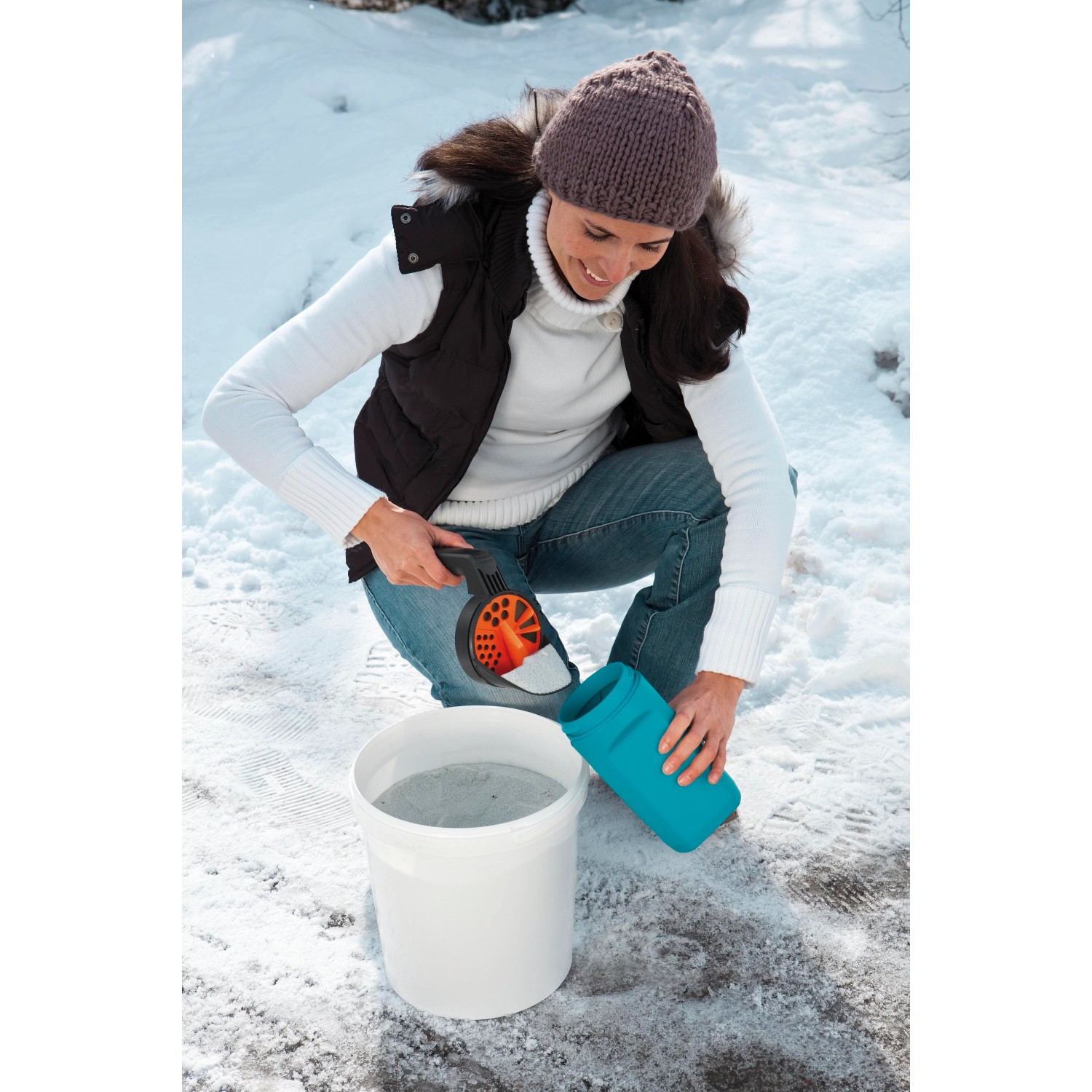 Frau befüllt Gardena Kleinstreuer S (türkis) mit Streugut aus Eimer. Streuwagen für Winterdienst.